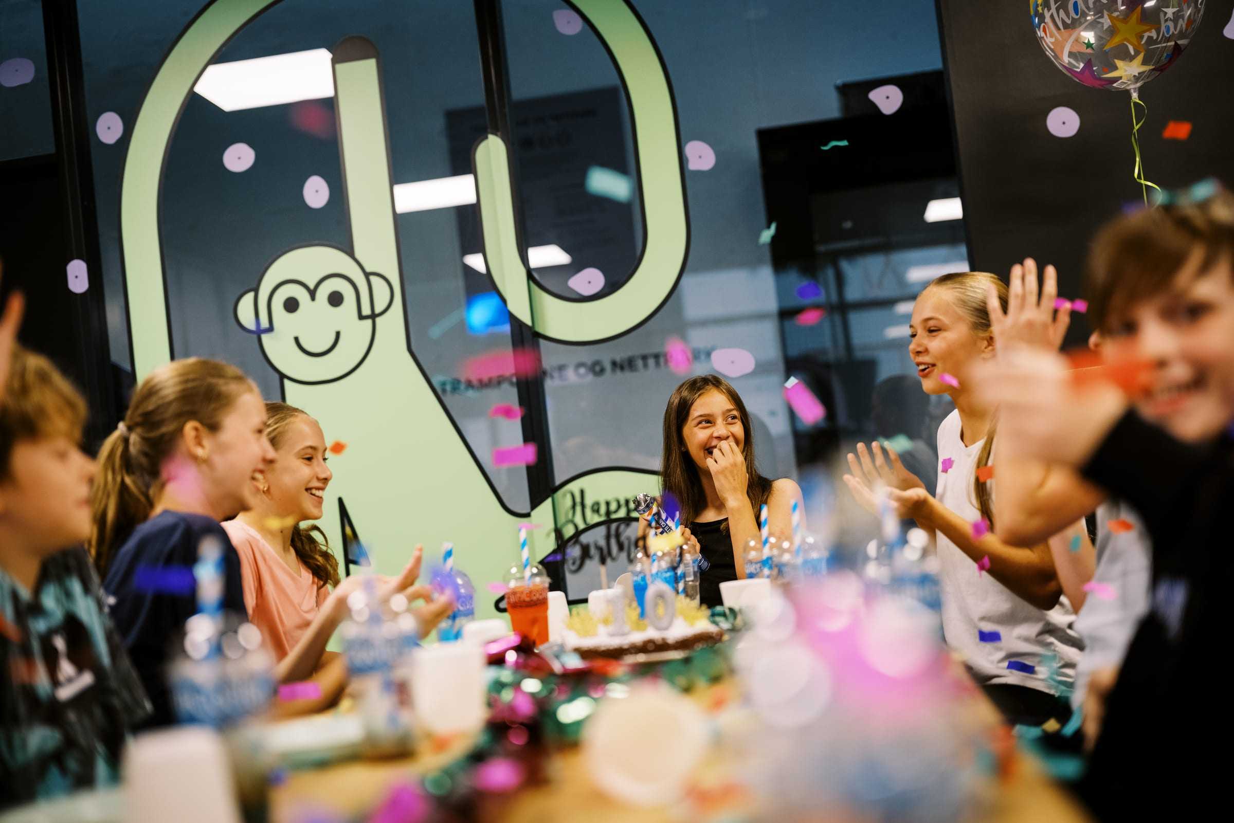 Confetti and laughter around the birthday table in front of the monkey mascot on the window
