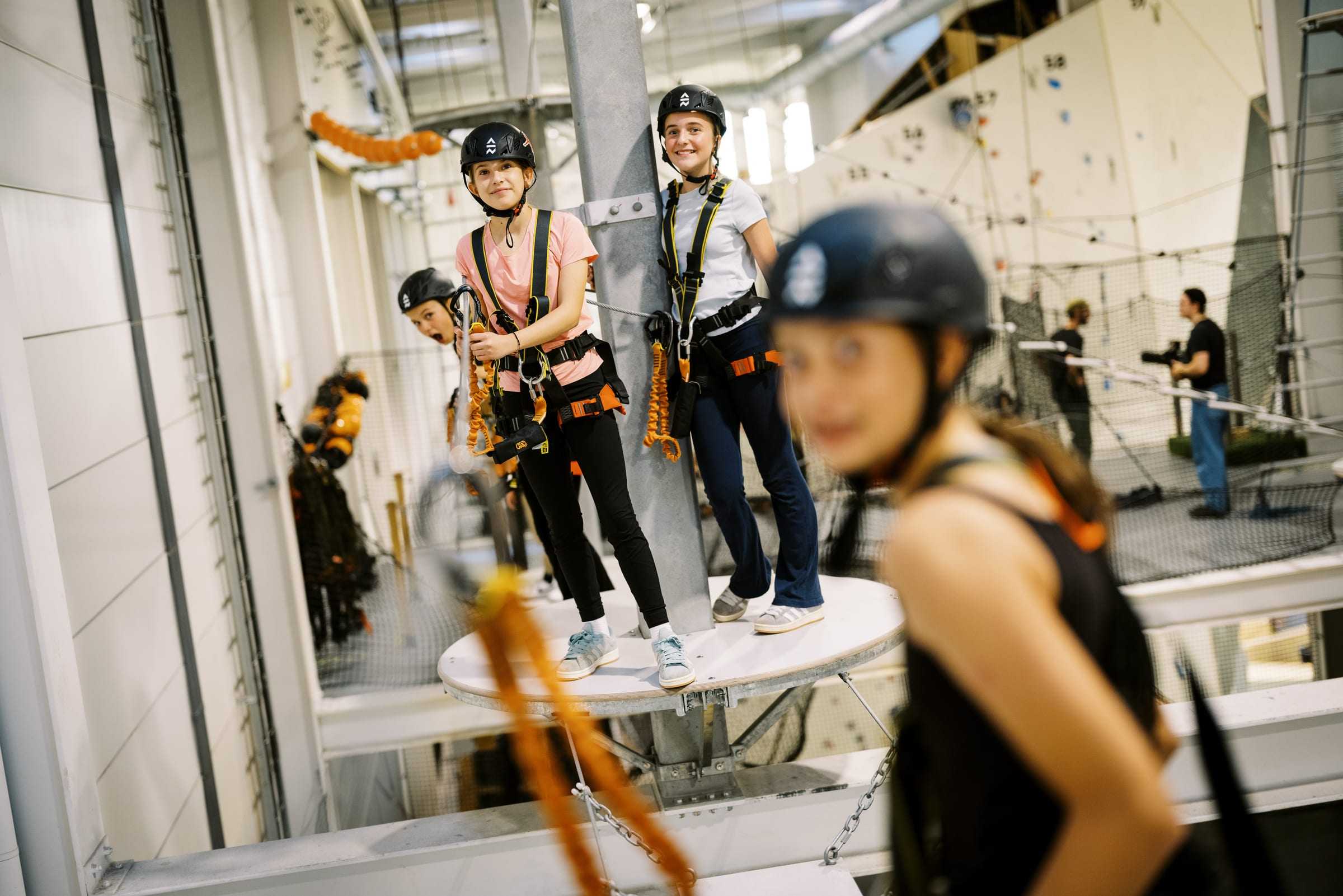 Two girls in harnesses and helmets smiling from a platform on the Via Ferrata course
