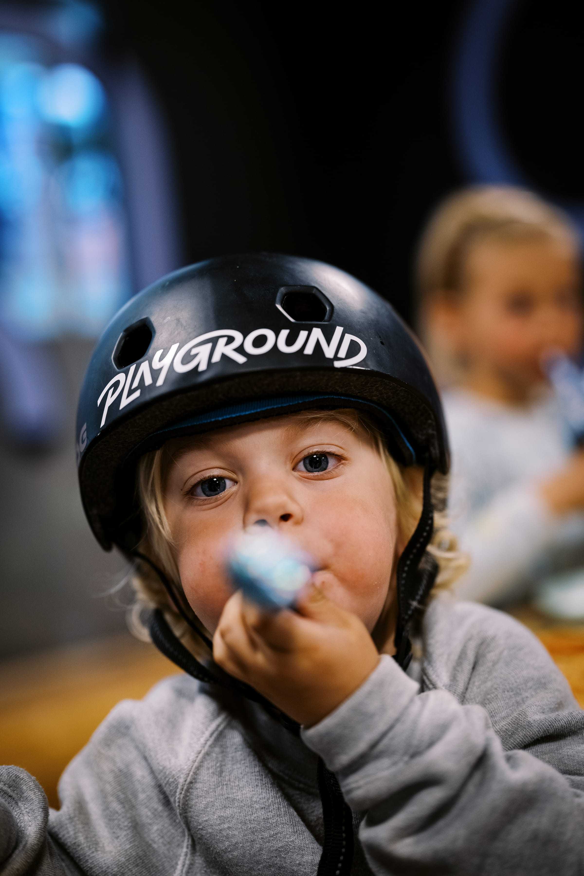 A little boy in a Playground helmet blowing a party horn
