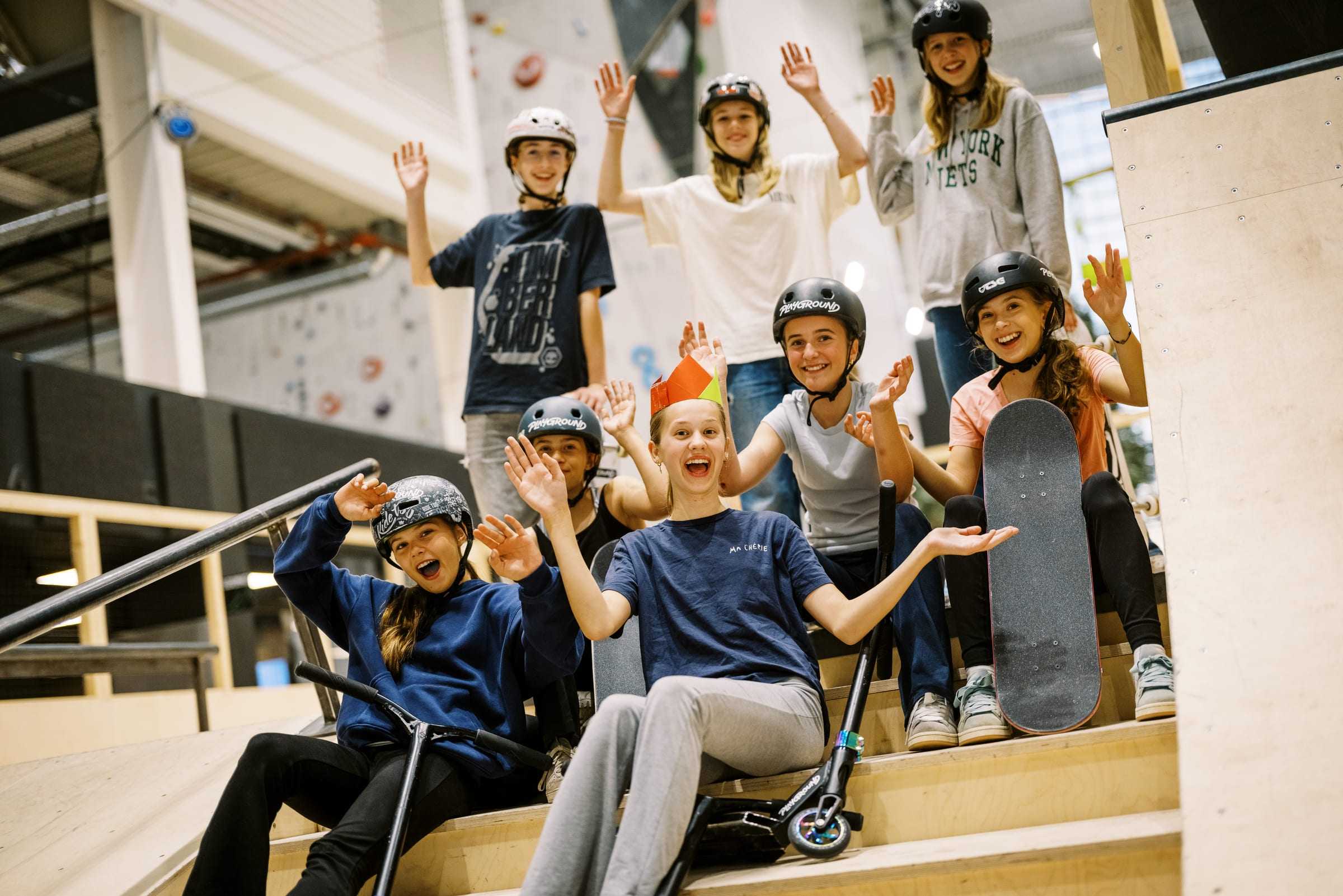 The birthday group waving from the skate park stands with boards, scooters and a paper crown