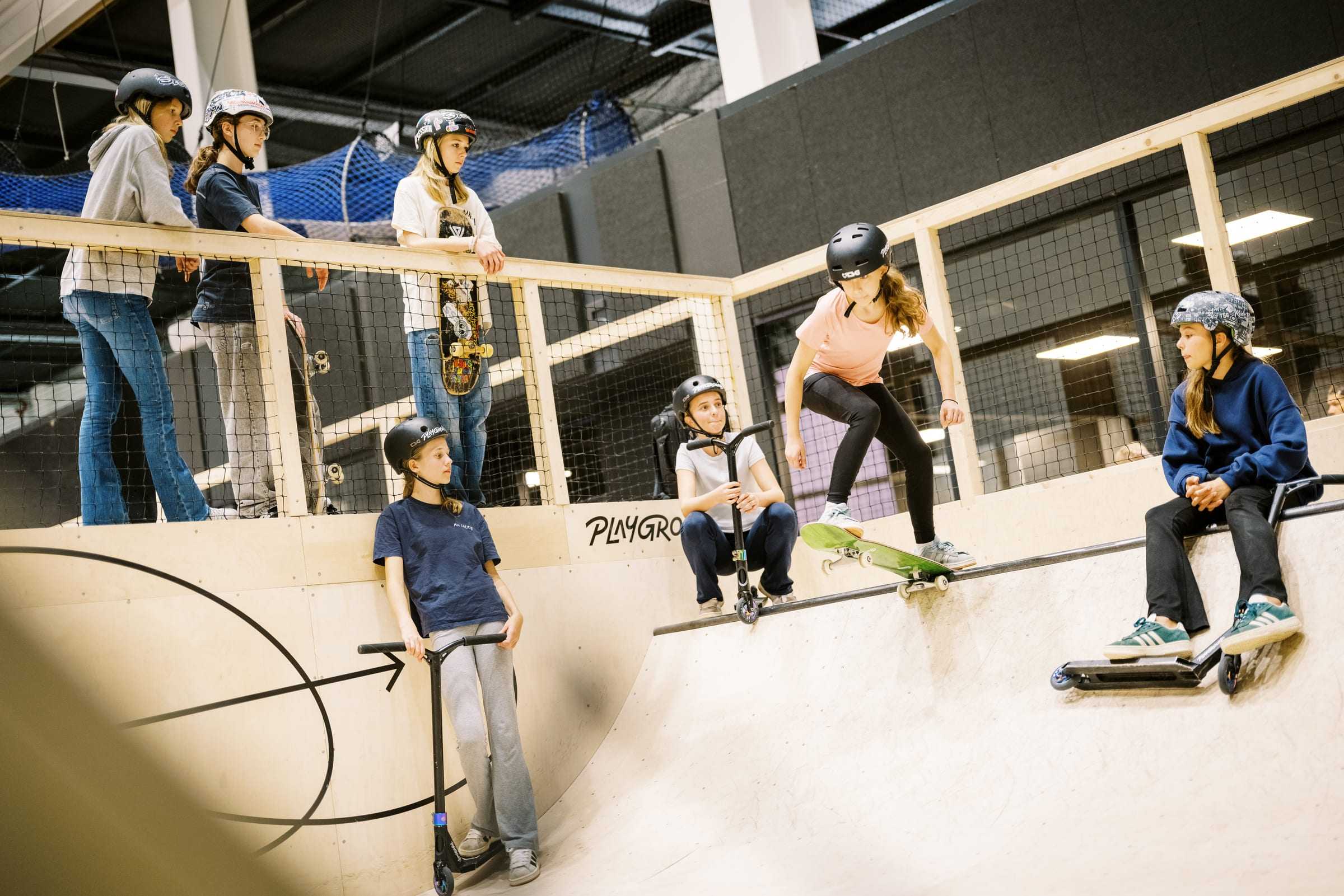 A girl drops into the bowl on a skateboard while her friends watch from the edge