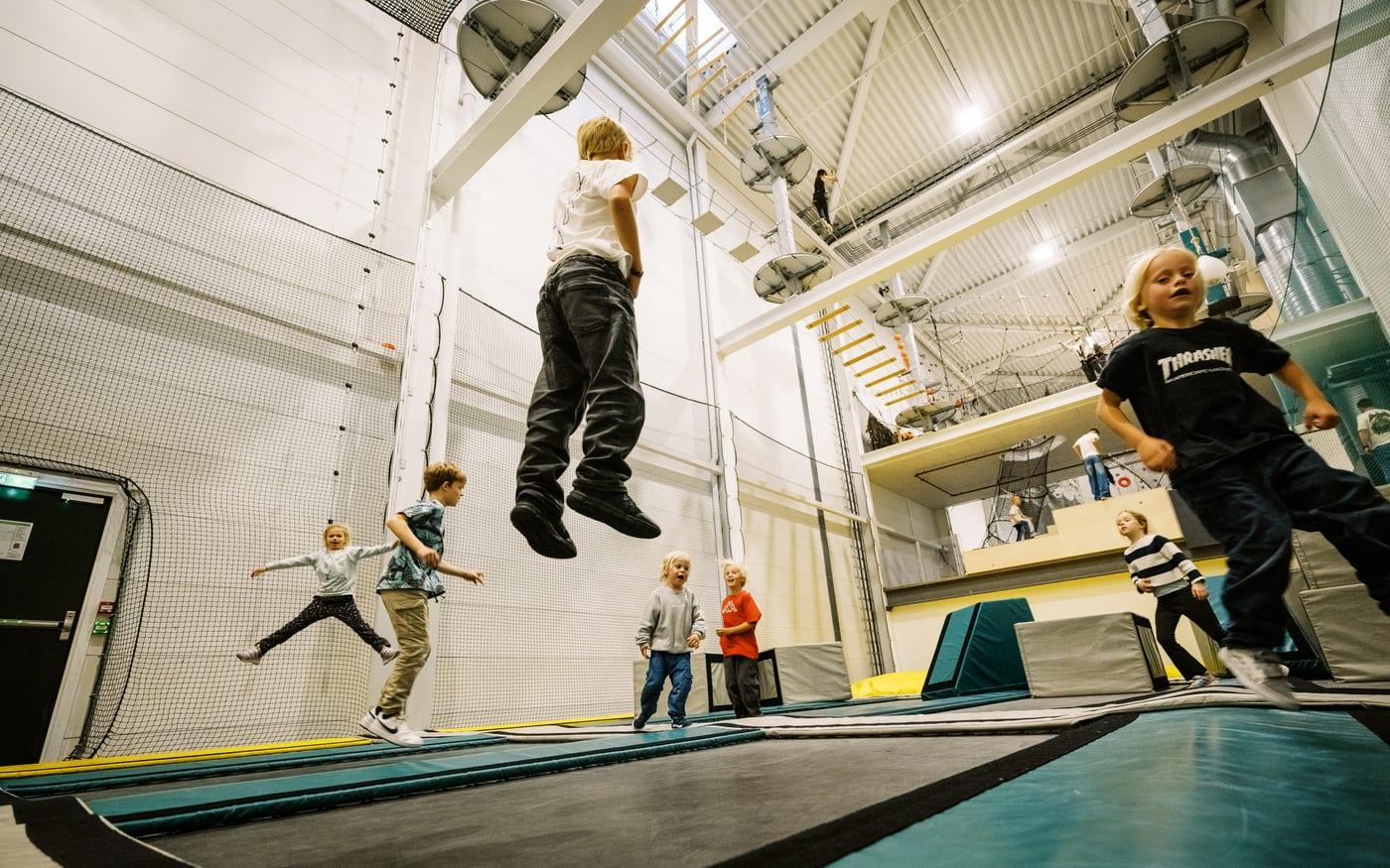 Gutt svever høyt over trampolinene mens andre barn hopper rundt ham
