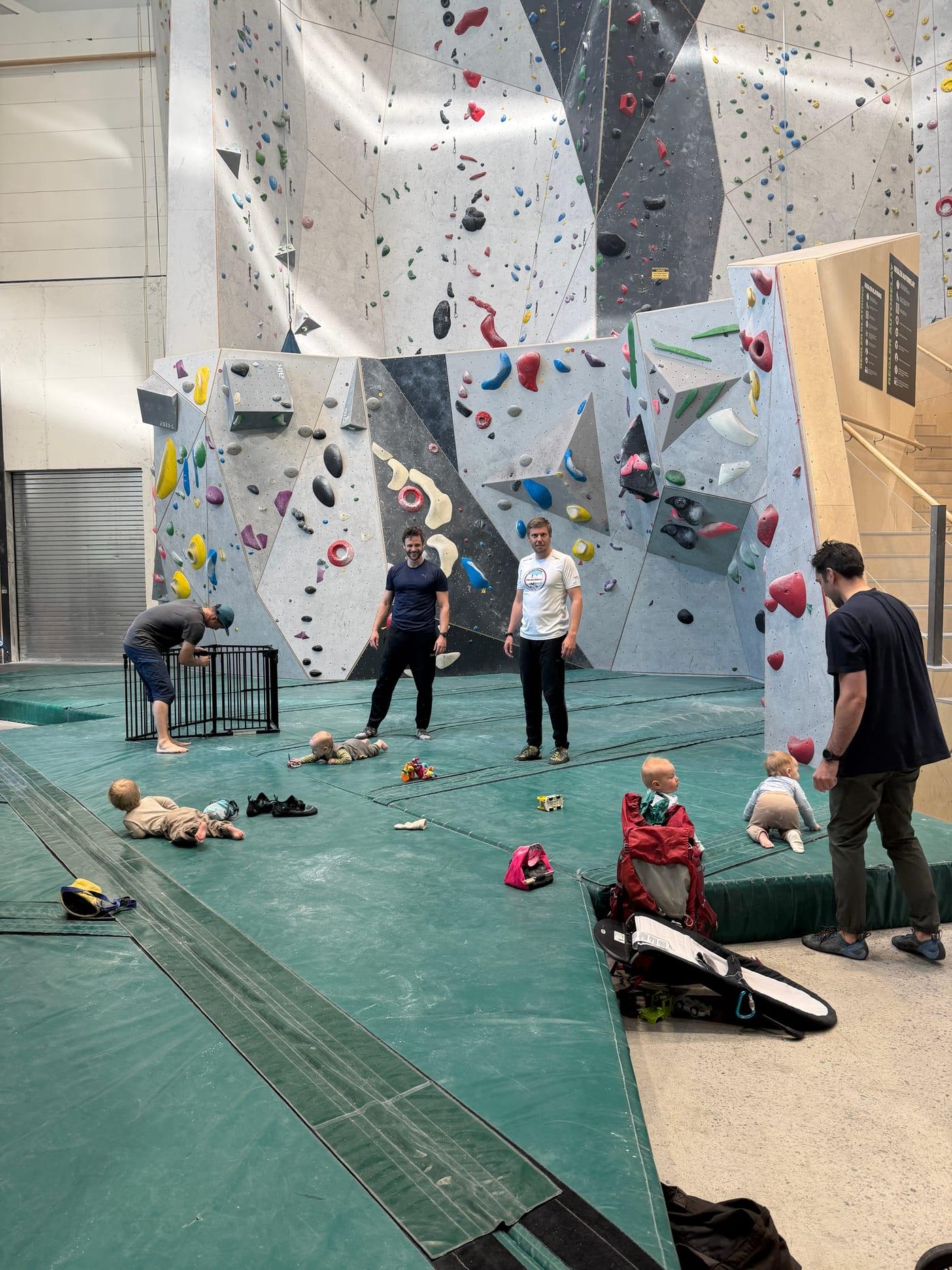 Parents and babies gathered on the mat in front of the bouldering wall at parent-and-baby climbing